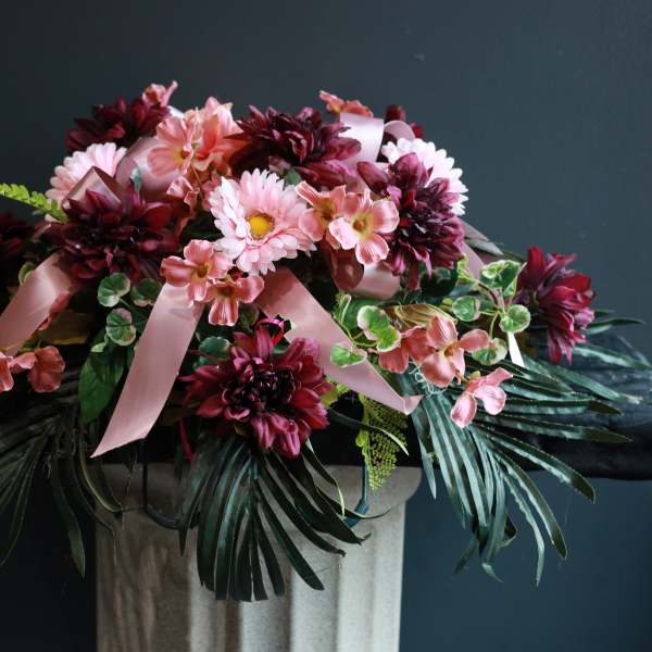 Pink and burgundy floral arrangement with ribbon on a pedestal