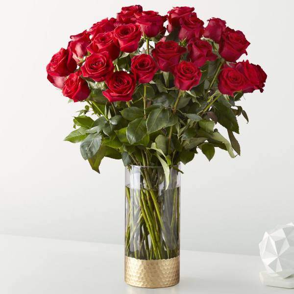 Red roses arranged in a clear glass vase with a gold base