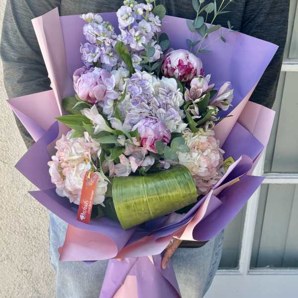 Handheld bouquet of pastel flowers wrapped in purple and pink paper