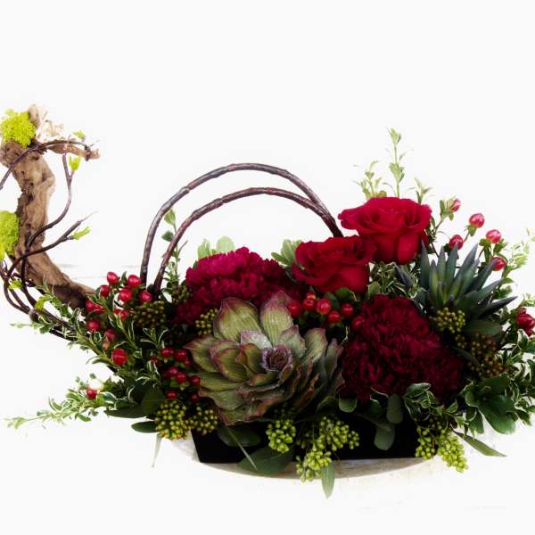 Red roses and burgundy blooms in a low basket with branches and berries