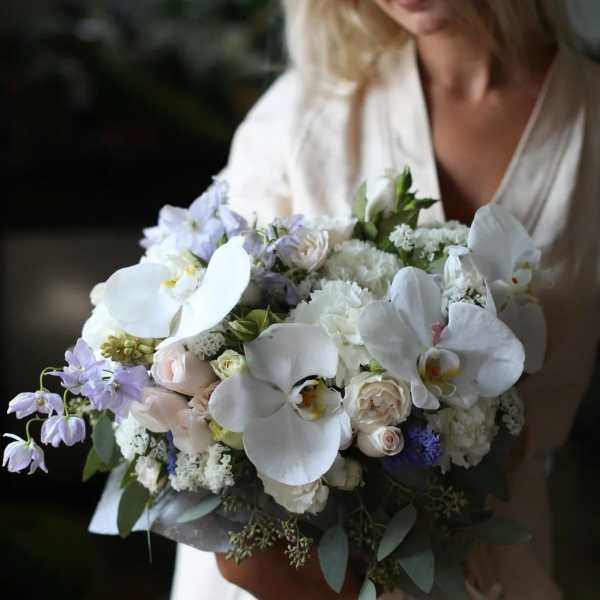 Woman holding a bouquet of white orchids and pale flowers