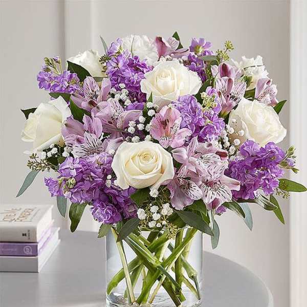 Bouquet of white roses and purple flowers in a clear glass vase