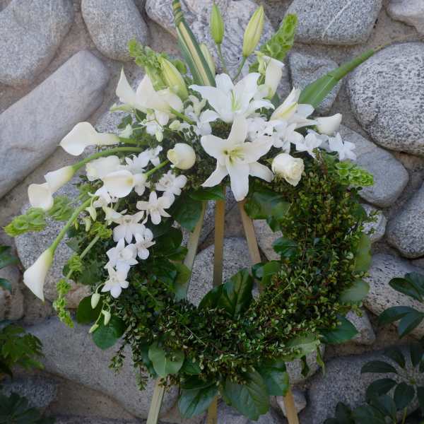 White floral wreath on a stand with lilies, calla lilies, and orchids