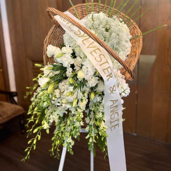 White floral standing spray with a wicker heart and ribbon