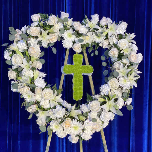 Heart-shaped white floral wreath with a green cross on an easel