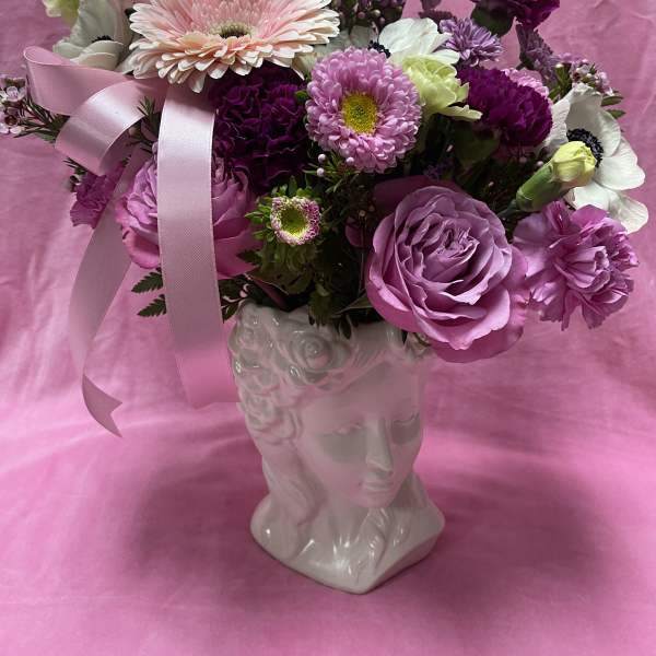 Pink and purple flower arrangement in a white face vase with ribbon