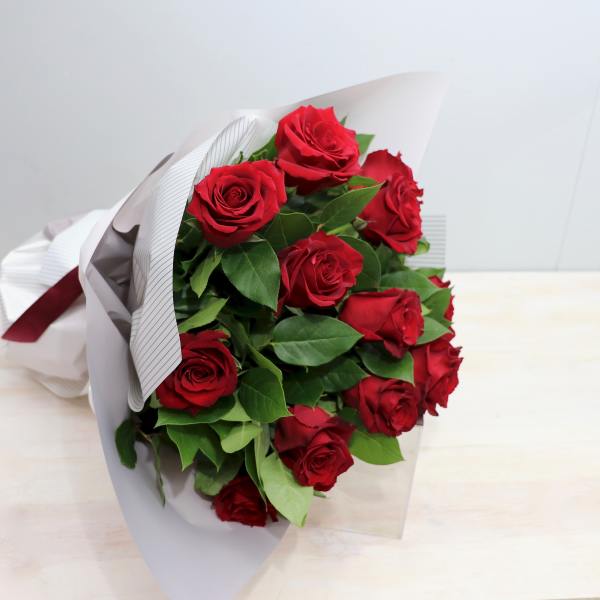 Hand-tied bouquet of red roses wrapped in white paper with a red ribbon
