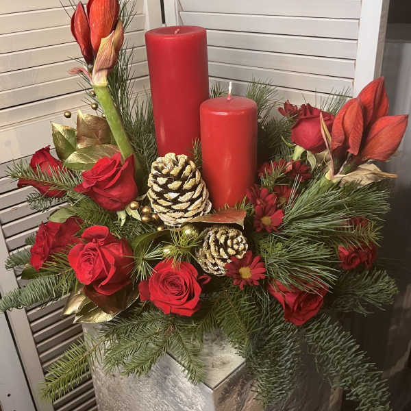 Red roses and amaryllis arranged with candles and pinecones in a festive centerpiece