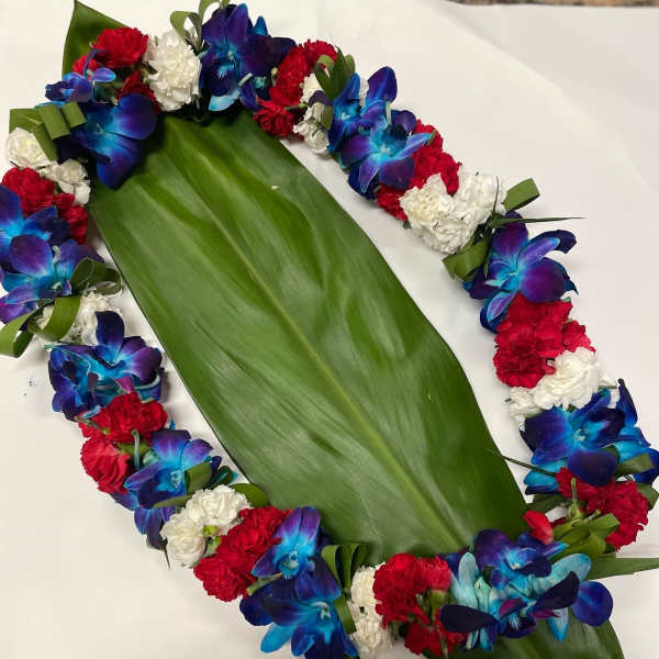 Floral lei with blue orchids, red carnations, and white flowers on a large green leaf