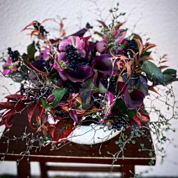 Purple floral arrangement in a white bowl vase