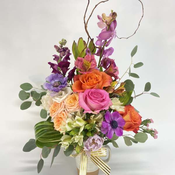 Colorful mixed flower arrangement in a white vase with ribbon