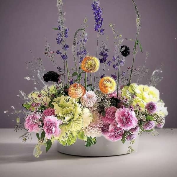 Mixed floral arrangement in a white bowl with pink, yellow, and purple blooms
