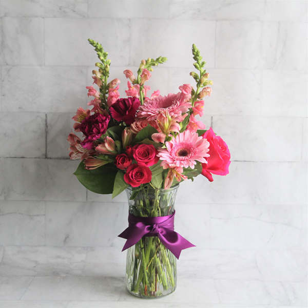 Pink mixed bouquet in a glass vase with a purple ribbon
