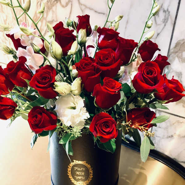 Red roses and white blooms arranged in a black hatbox