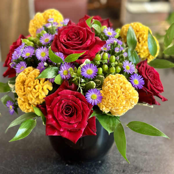 Bouquet of red roses, purple daisies, and yellow blooms in a black vase