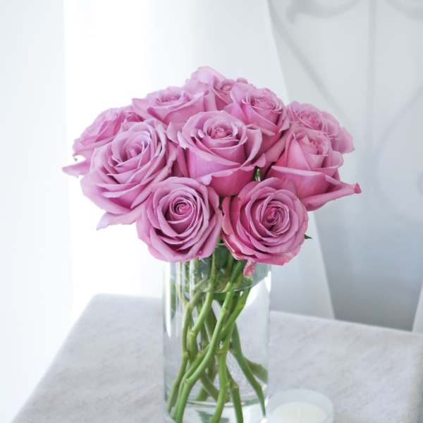 Pink roses arranged in a clear glass vase beside a small white candle