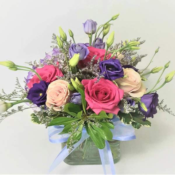 Pink, purple, and cream flowers in a glass vase with a blue ribbon
