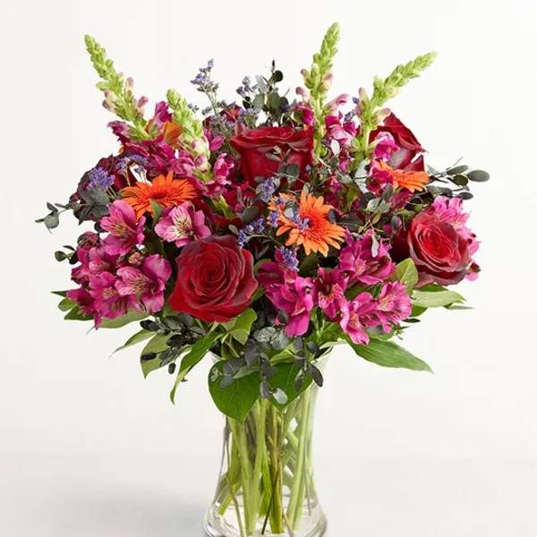Bouquet of red roses, pink alstroemeria, and orange daisies in a clear glass vase