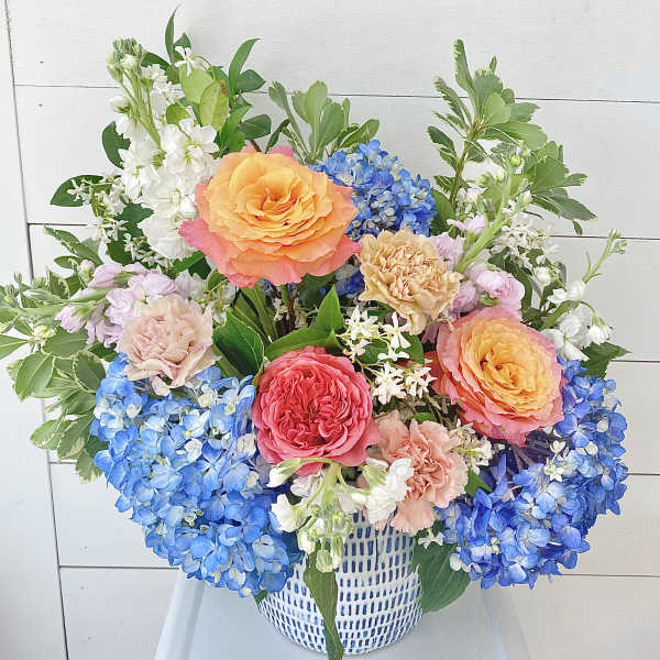 Colorful bouquet of roses, hydrangeas, and carnations in a white basket vase