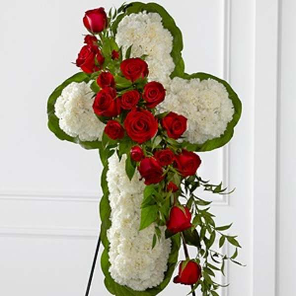 Cross-shaped floral tribute with red roses and white blooms on a stand