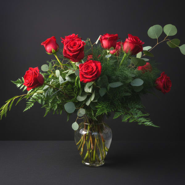 Red roses arranged in a clear glass vase with eucalyptus foliage