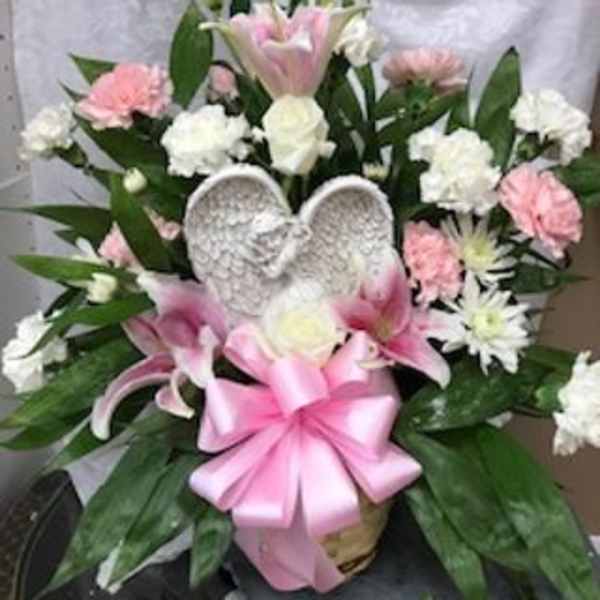 Pink and white floral arrangement with a pink ribbon and angel wings