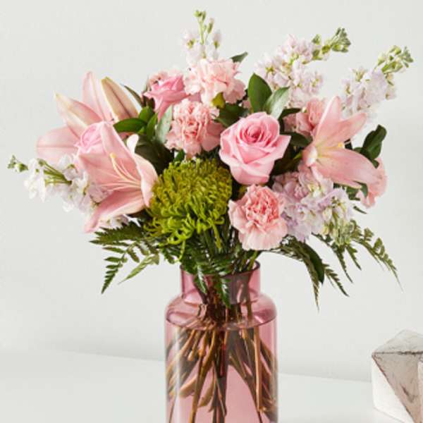 Pink bouquet of lilies, roses, and carnations in a pink glass vase