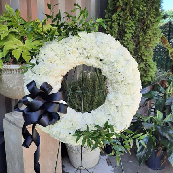 White floral wreath with a black ribbon bow on a stand