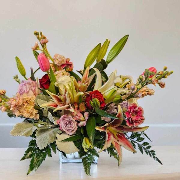 Mixed bouquet in a clear glass vase with lilies, roses, and pink blooms