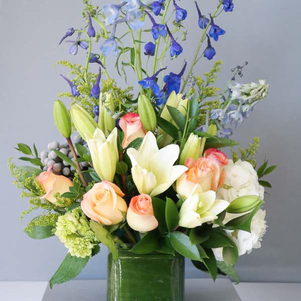 Mixed bouquet of lilies, roses, and blue delphinium in a glass vase