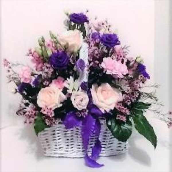 Pink and purple flower arrangement in a white wicker basket with a purple ribbon