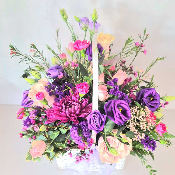 Basket arrangement of purple, pink, and peach flowers with a white handle