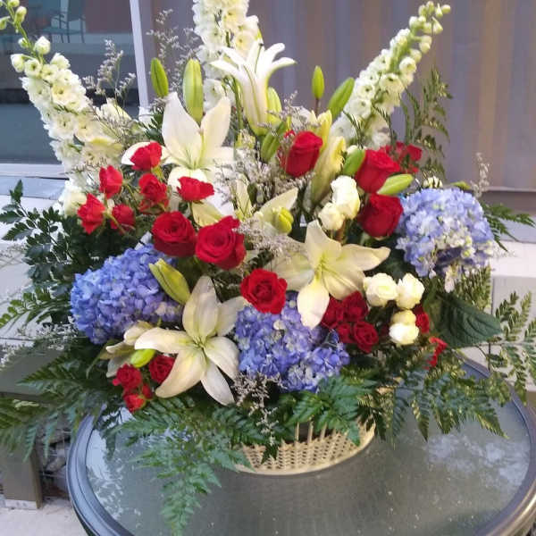 Large floral arrangement with red roses, white lilies, and blue hydrangeas in a basket