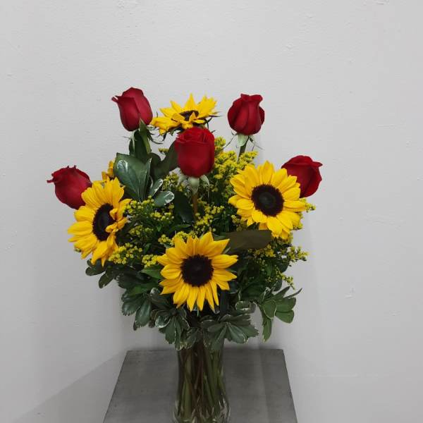 Bouquet of red roses and yellow sunflowers in a clear glass vase