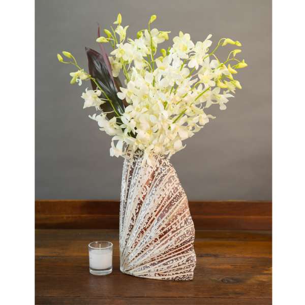 White orchid arrangement in a patterned vase beside a small candle