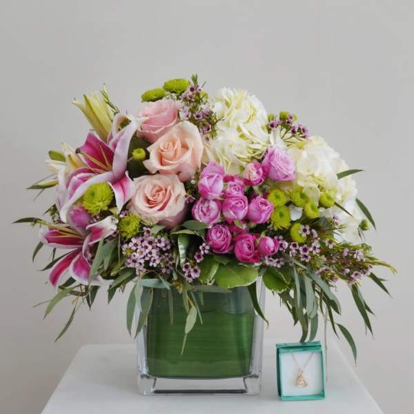 Mixed pink and white flower arrangement in a glass vase with a small necklace box beside it