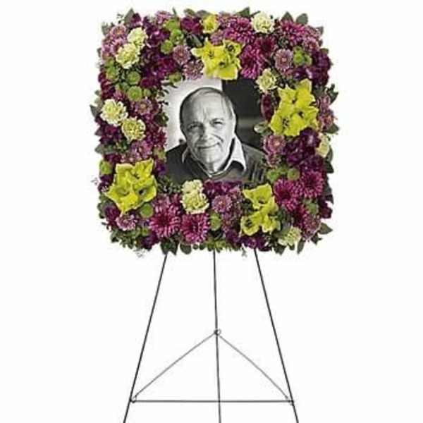 Standing funeral wreath of purple and yellow flowers around a portrait