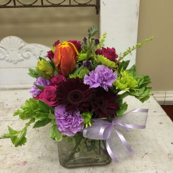 Mixed bouquet in a square glass vase with a lavender ribbon