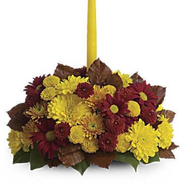 Yellow candle in a low arrangement of red and yellow chrysanthemums