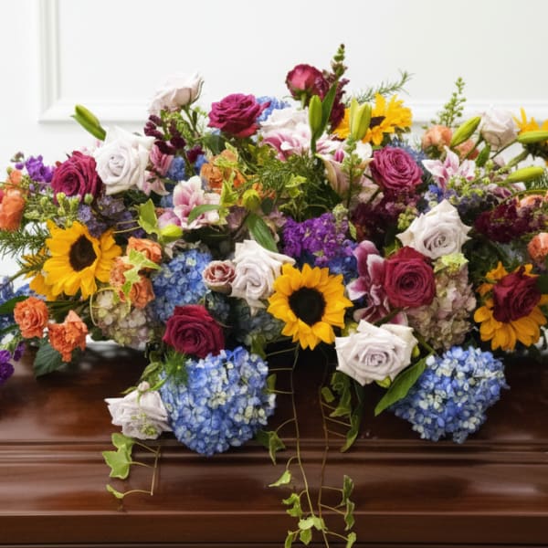 Colorful floral casket spray with roses, sunflowers, and hydrangeas