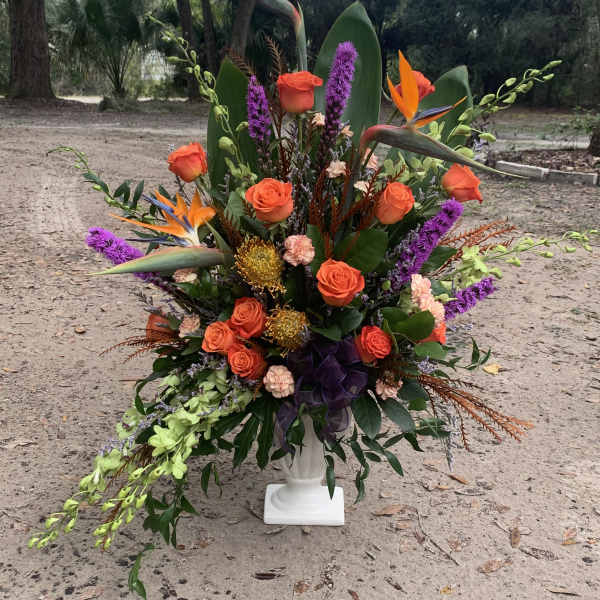 Tropical floral arrangement with orange roses and bird of paradise in a white pedestal vase