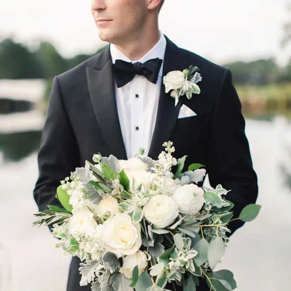Man in tuxedo holding a white bridal bouquet with greenery