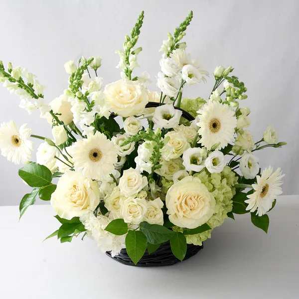 White floral arrangement in a black basket with roses and daisies