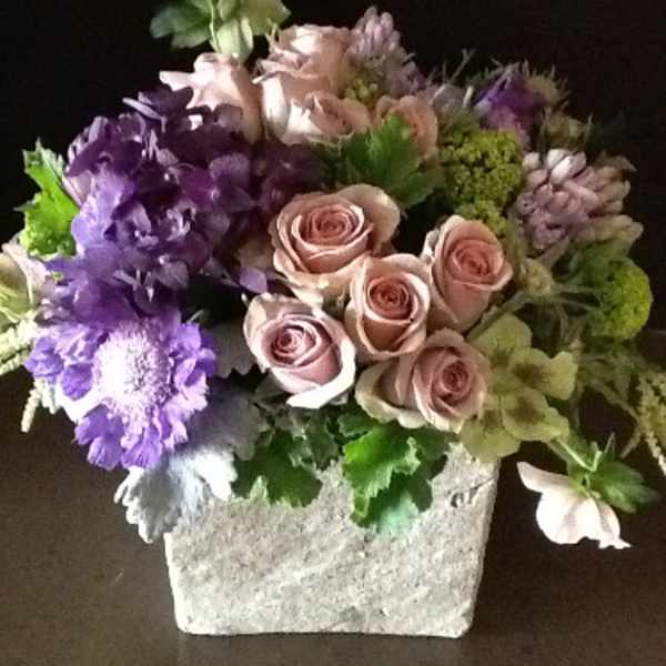 Mixed bouquet of pink roses and purple flowers in a square stone vase