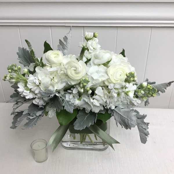 White floral arrangement in a clear rectangular vase with silver foliage