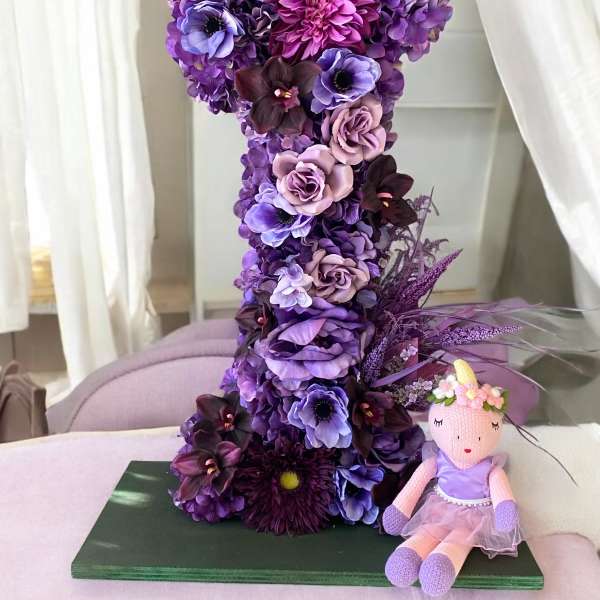 Purple floral number 1 arrangement with a small doll beside it