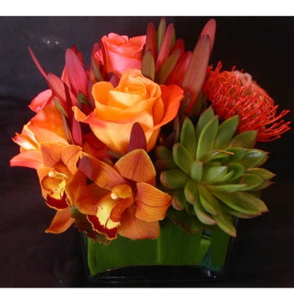 Orange and pink bouquet with orchids and roses in a glass vase
