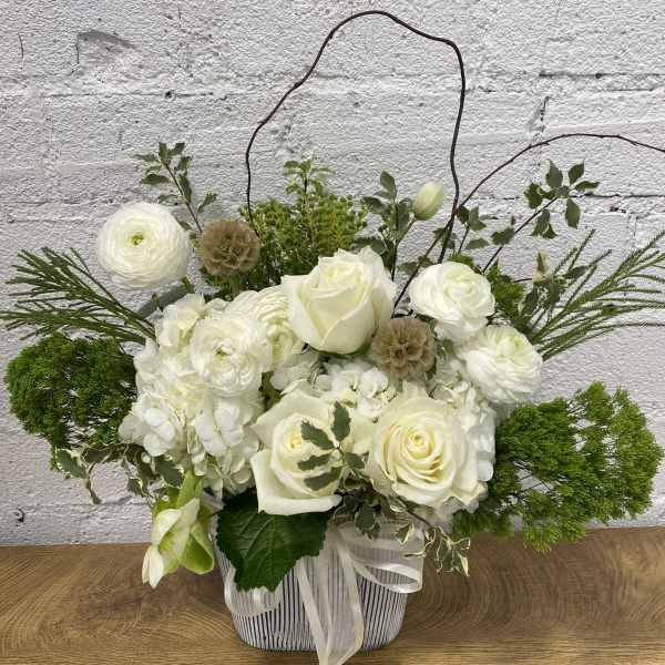 White roses and ranunculus in a striped basket with a ribbon handle