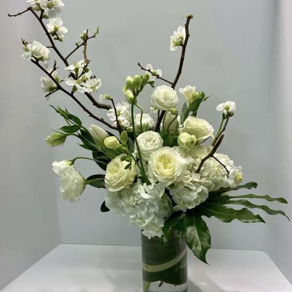 White floral arrangement in a clear glass vase with branching stems