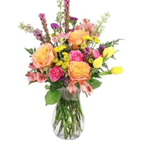 Mixed bouquet of peach, pink, yellow, and purple flowers in a clear glass vase